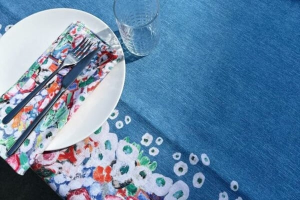 The blue tablecloth seen from above, its floral border running beside a white plate and glass.