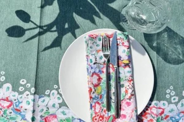 The celadon tablecloth laid for a single place setting, a floral napkin folded on a white plate.