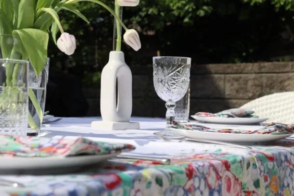 The white tablecloth on an outdoor table set with tulips, cut glass, and floral napkins.